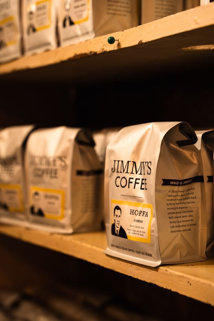 Close-up of Jimmy's Coffee bags neatly arranged on wooden shelves.